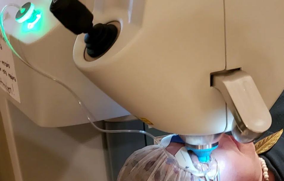 A patient lying beneath an eye-surgery laser, its green targeting light lit.