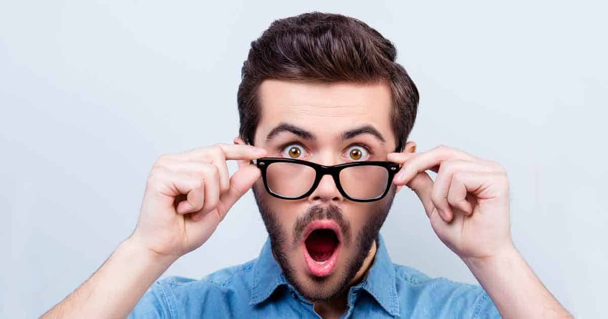 A man lowers his glasses, eyes wide and mouth open.